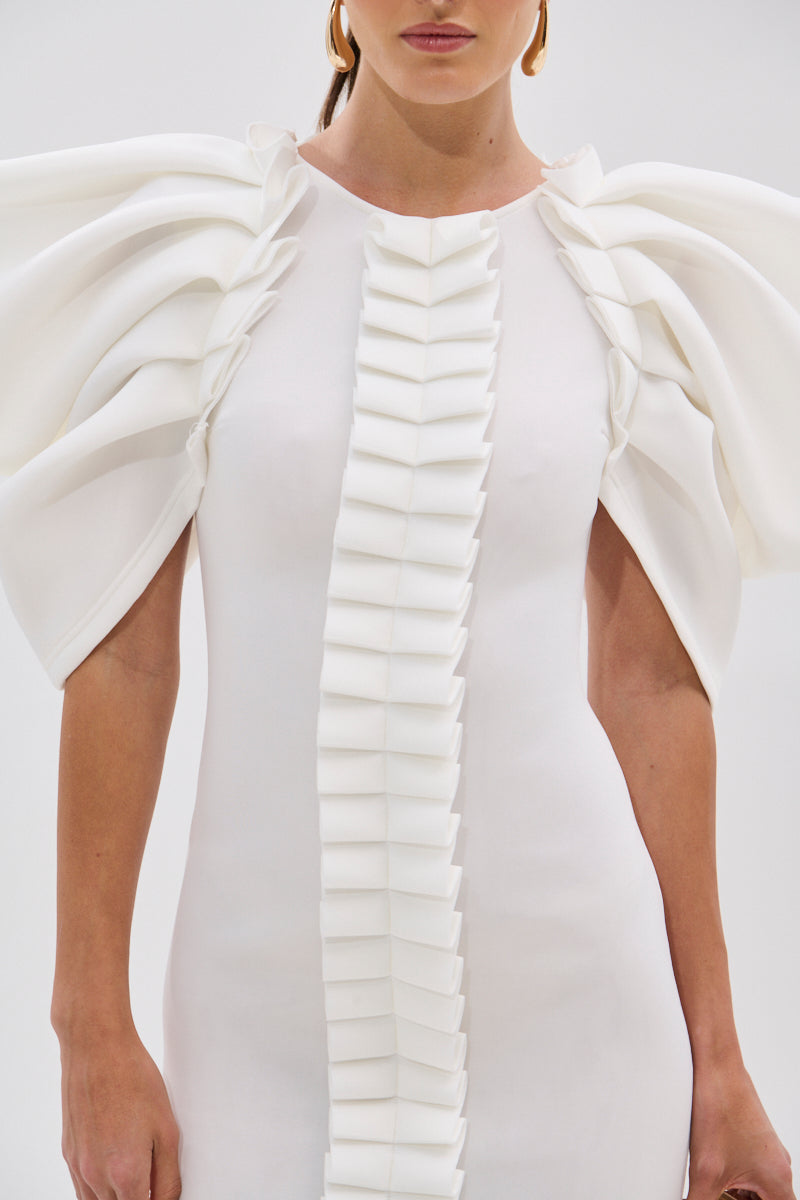 A woman wears the PURE JOY MIDI DRESS WITH DRAMATIC SLEEVE IN WHITE, featuring sculptural ruffled sleeves and structured folded details down the front. The image is cropped at her shoulders and mid-thigh.