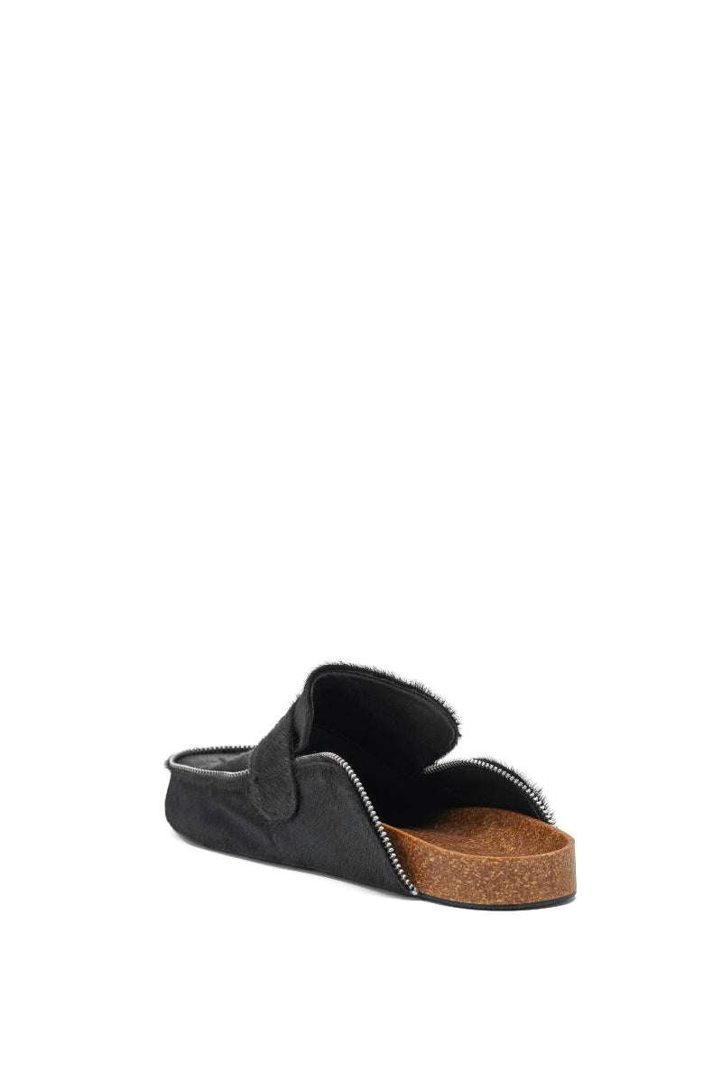 The AZALEA WANG LIMERICK BLACK METAL EMBELLISHMENT FLAT is a black slip-on, backless mule sandal with a cork sole, fuzzy interior lining, and zipper-edged detail, displayed against a white background. 5