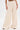 Wearing the SYDNEY TEXTURED PALAZZO PANT in cream, with a high-rise, wide-leg silhouette and drawstring waist, a person stands against a plain white background, showing only the lower half of their body.