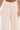 Wearing the SYDNEY TEXTURED PALAZZO PANT in cream, which features textured fabric with a subtle swirling pattern and wide-leg silhouette, a person displays their midriff, showing a belly button piercing and part of a tattoo.