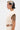 A person with short, slicked-back blonde and black hair stands in profile, wearing the SYDNEY TEXTURED BLOUSE with ruched cinched detail and matching bottoms, accessorized with earrings and showing a detailed arm tattoo.
