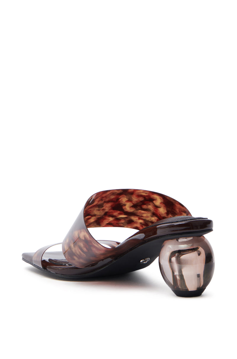 The AZALEA WANG LIRIO Brown Ball Heel Sandal features a stylish brown faux patent leather strap with a wide tortoiseshell pattern and a unique transparent spherical novelty heel, elegantly angled to highlight both the strap and the striking design.