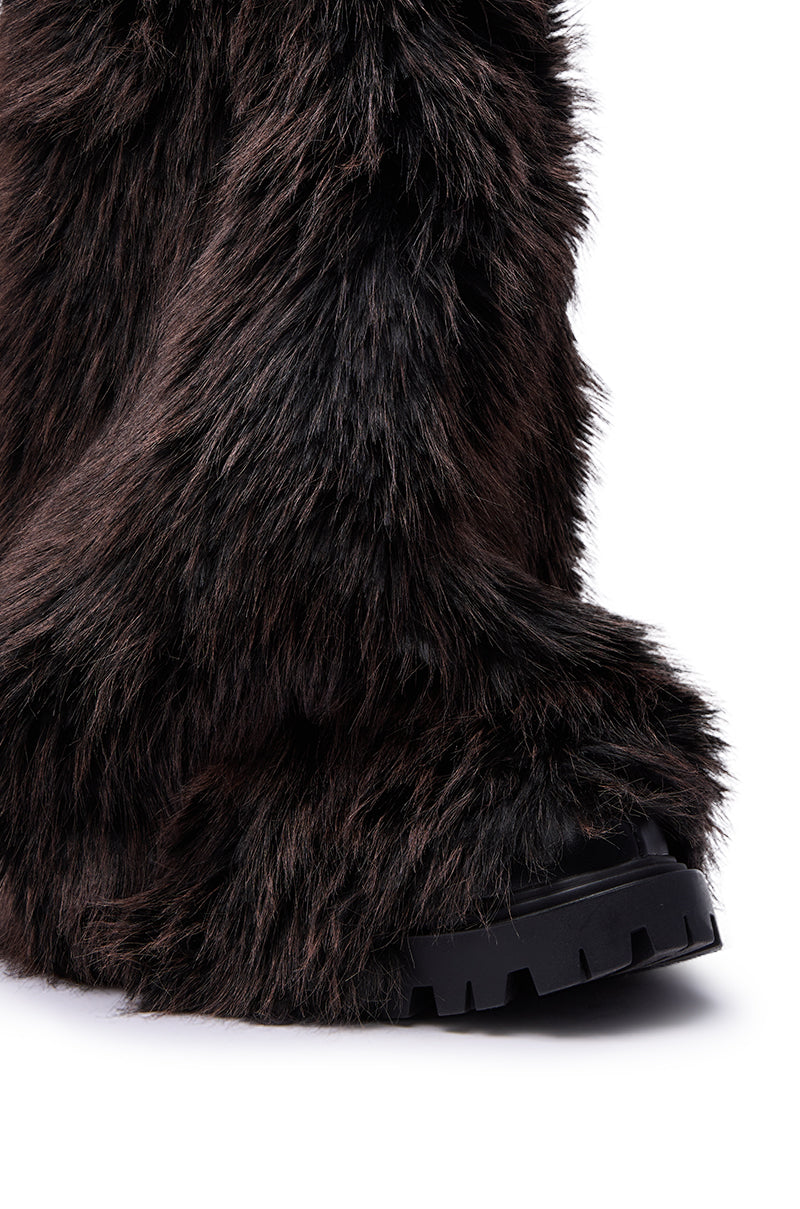Close-up of a foot wearing the AZALEA WANG LISBOA BROWN FUR FOLD OVER BOOT, featuring thick brown fur and a black rugged sole, against a white background.