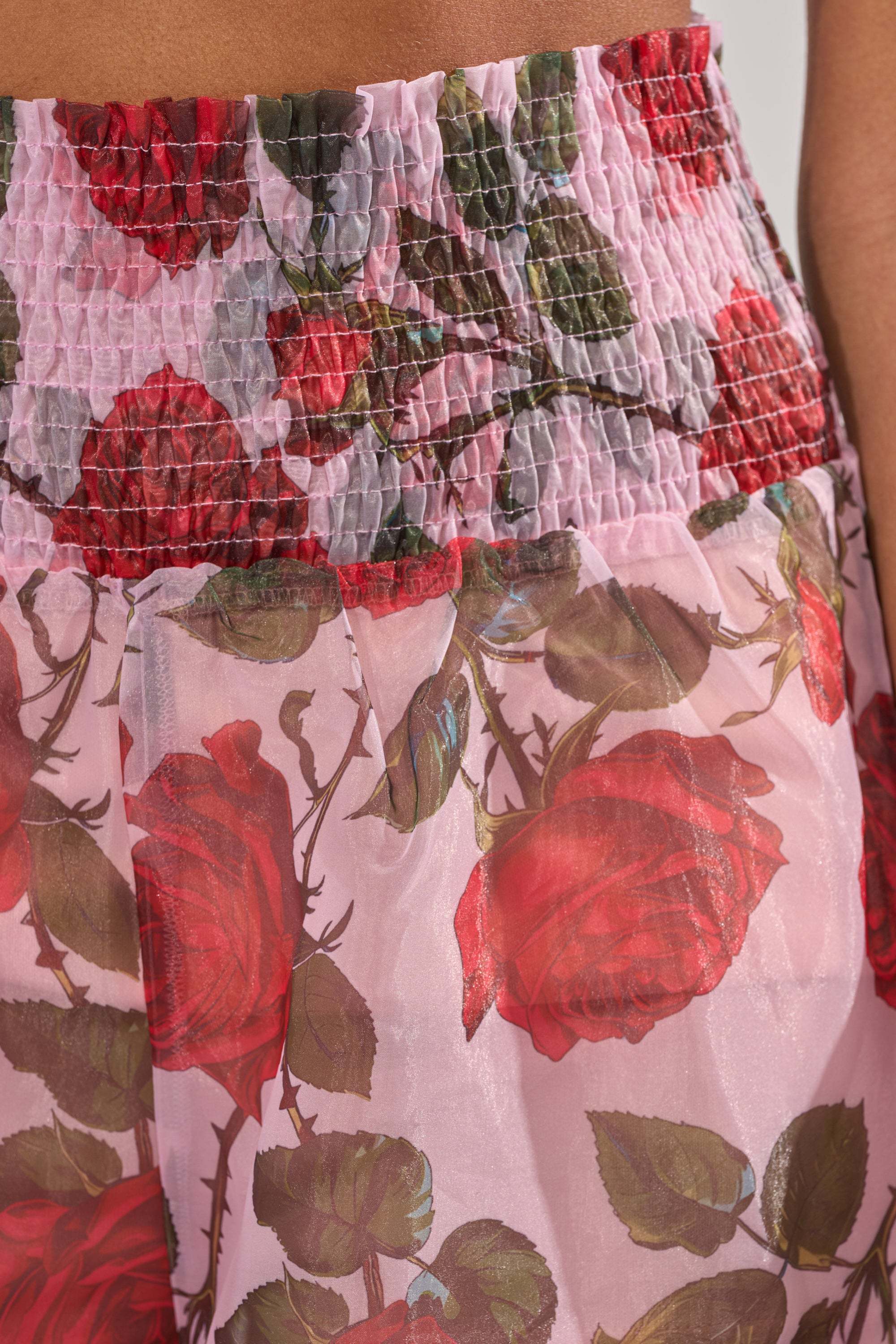 Close-up of the PRETTY GIRL FLORAL TROUSER, showcasing a pink design with a high-rise smocked waistband and vibrant red rose with green leaf print on sheer, lightweight fabric. 6