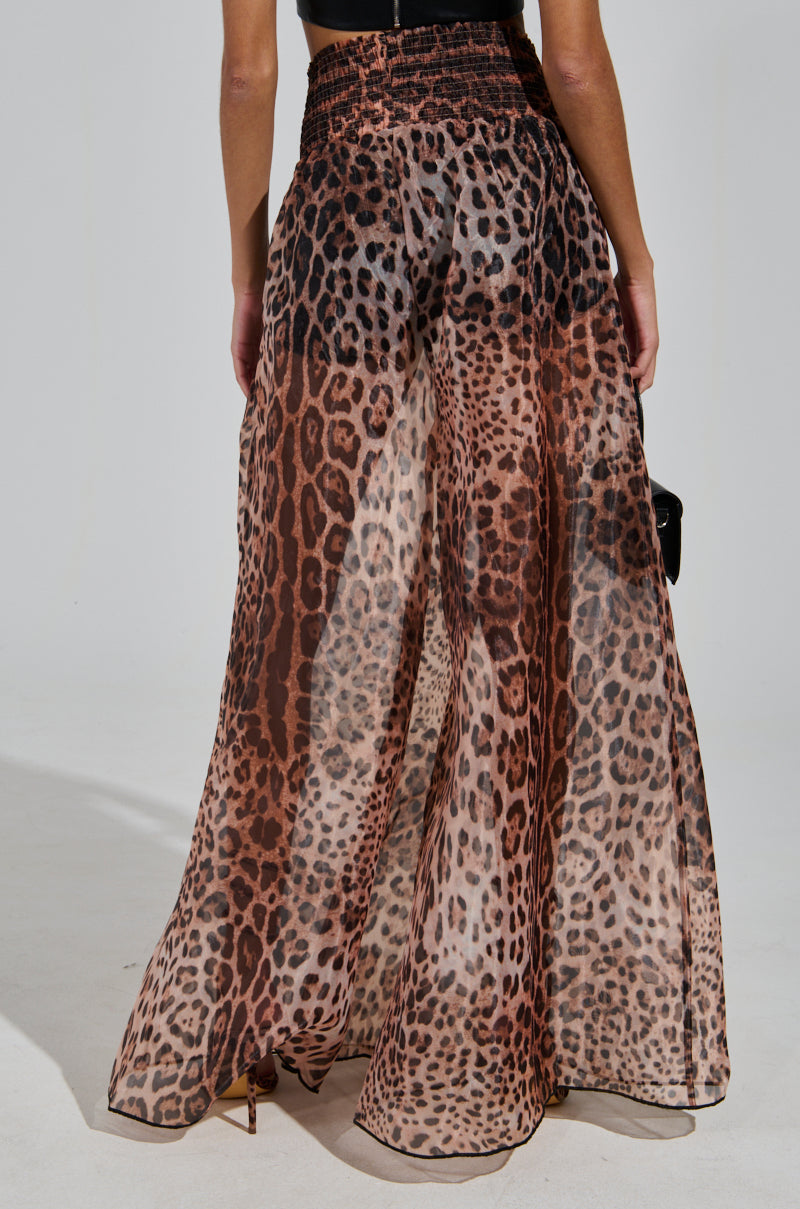 A person wearing the CHEETAH GIRL PALAZZO PANT stands with their back to the camera. They hold a small black handbag and wear heels, showcasing a chic and stylish look.