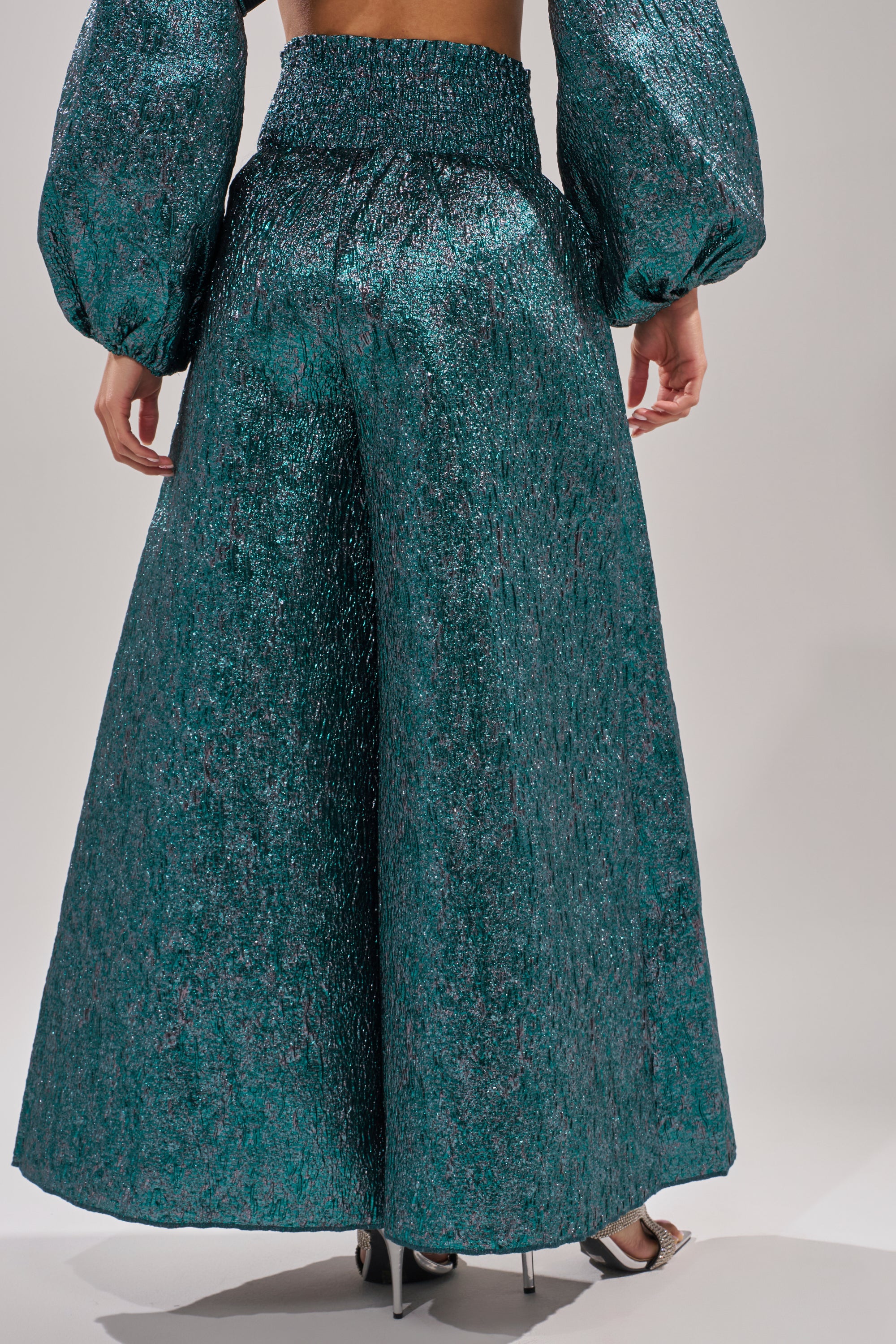 A person wearing the "ITS TIME TO CELEBRATE PALAZZO PANT" in teal brocade with matching voluminous sleeves and high-heeled sandals is shown from the back, displaying the textured, shimmering fabric. 4