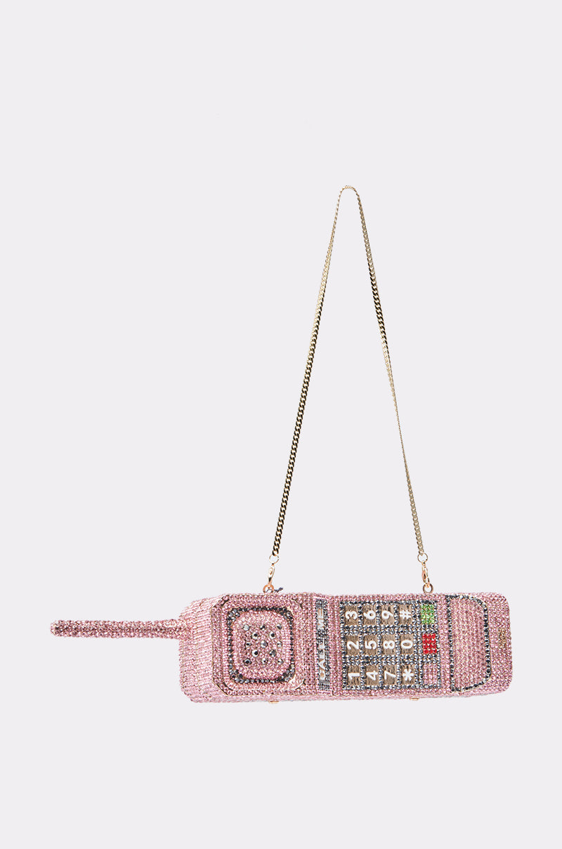 The HIT MY LINE BLING PURSE is a Y2K-inspired pink rhinestone handbag shaped like a vintage cell phone, featuring detailed keypad buttons, a playful antenna, and a long gold chain strap. 4