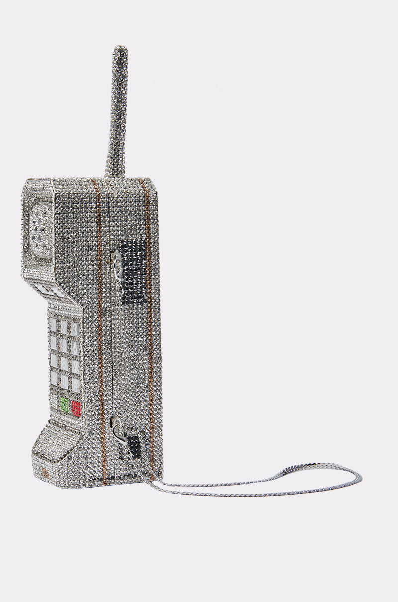 The CALL ME BLING CLUTCH is a vintage-inspired phone-shaped purse adorned with sparkling rhinestones and a silver chain, shown against a white background—an eye-catching accessory for any glamorous event.