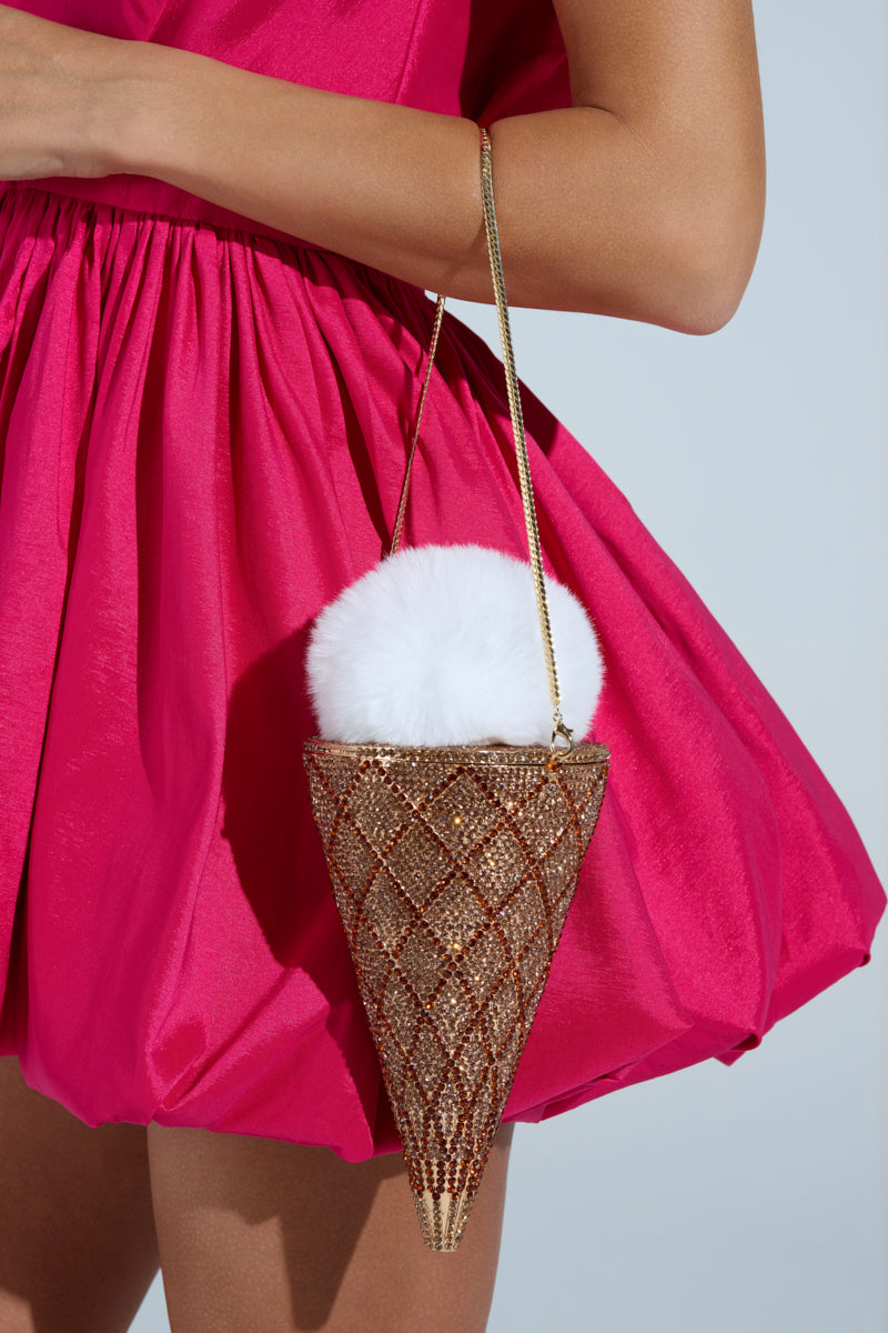 A person in a pink pleated dress holds the LICK IT UP FAUX FUR ICE CREAM BAG, featuring a rhinestone waffle cone with a lattice pattern and a top resembling a scoop of white, fluffy faux fur.