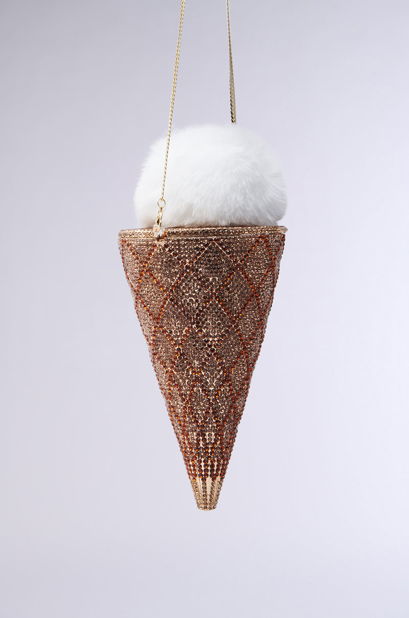 The LICK IT UP FAUX FUR ICE CREAM BAG is a beaded, cone-shaped handbag with a diamond pattern of gold beads resembling a rhinestone waffle cone. A white pom-pom on top mimics ice cream, and it hangs from a thin gold chain against a plain background.
