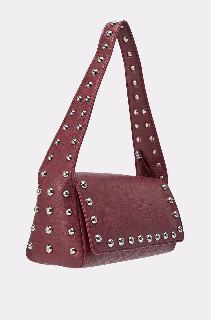 The LOLA STUDDED PURSE is a maroon shoulder bag with a wide strap and rectangular flap, featuring rows of silver studs along the strap, sides, and flap, shown against a plain light background. 2