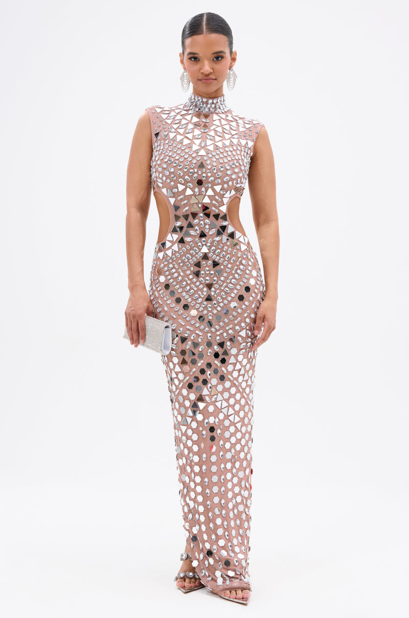 A woman models the QUEEN OF EVERYTHING MIRRORED MAXI DRESS IN SILVER— a fitted, sleeveless maxi with silver geometric patterns, rhinestone mirror appliqués, side cutouts—styled with dangling earrings, strappy heels, and a silver clutch against a white background.