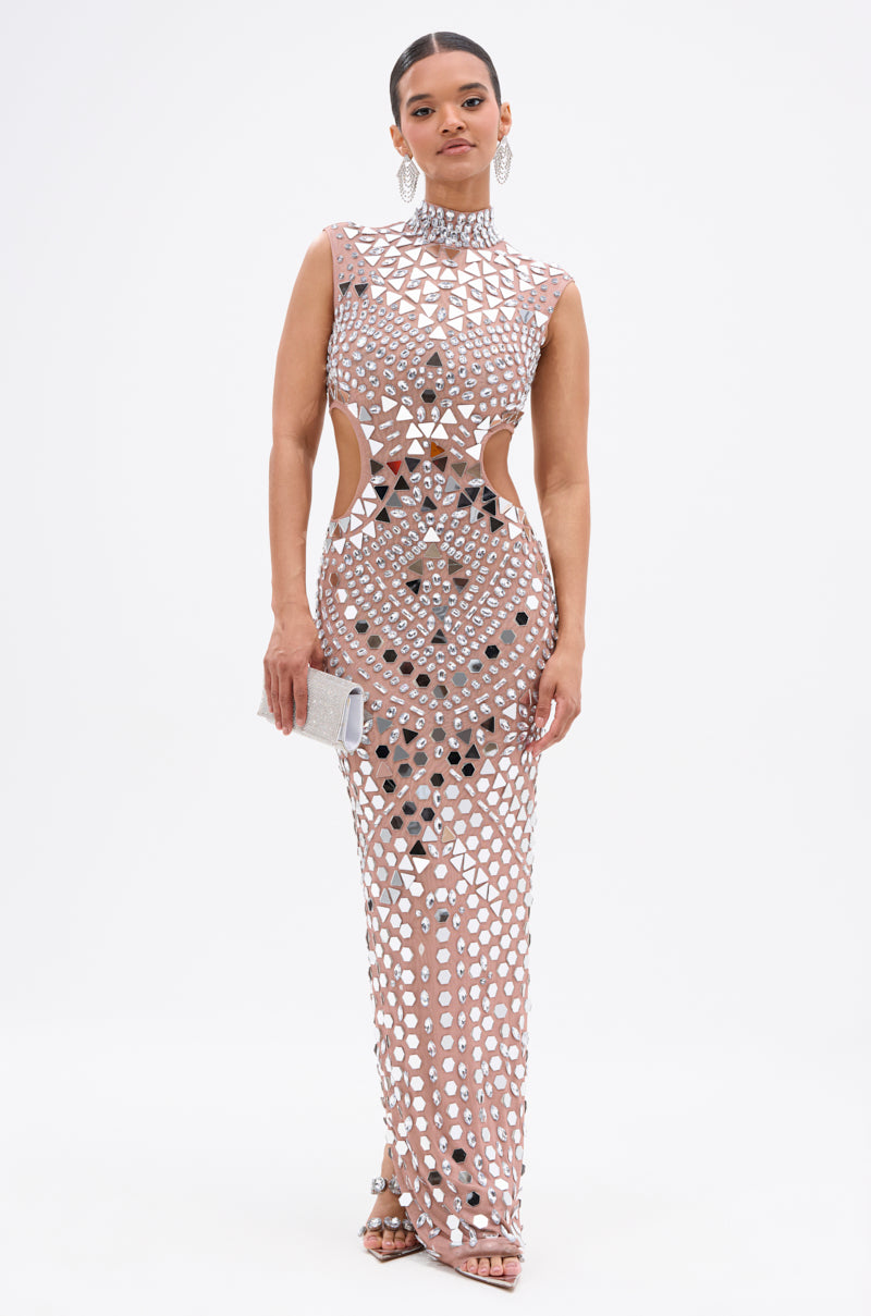 A woman faces forward in the QUEEN OF EVERYTHING MIRRORED MAXI DRESS IN SILVER, featuring a sleeveless silhouette, silver geometric mirror accents, cut-out sides, and accessorized with a small silver clutch, hoop earrings, and strappy heels.