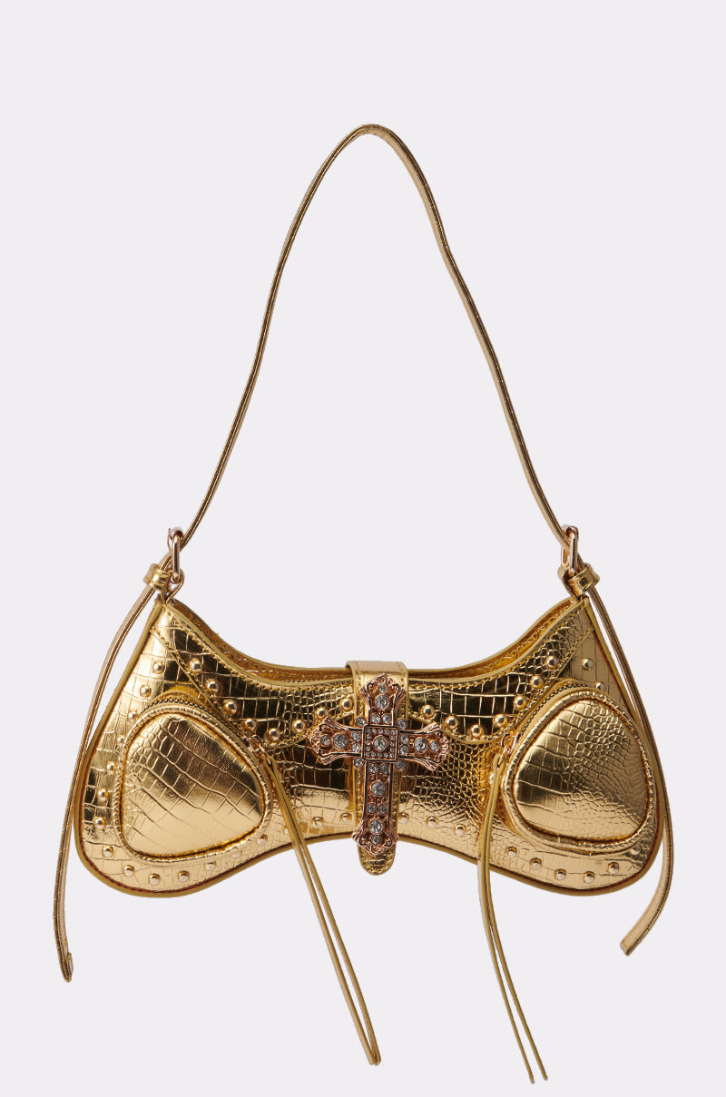 The TOO ROYAL CROSS PURSE is a gold, crocodile-textured handbag with a curved, structured shape, jeweled cross-shaped clasp, stud accents, and a thin shoulder strap set against a plain light background. 1