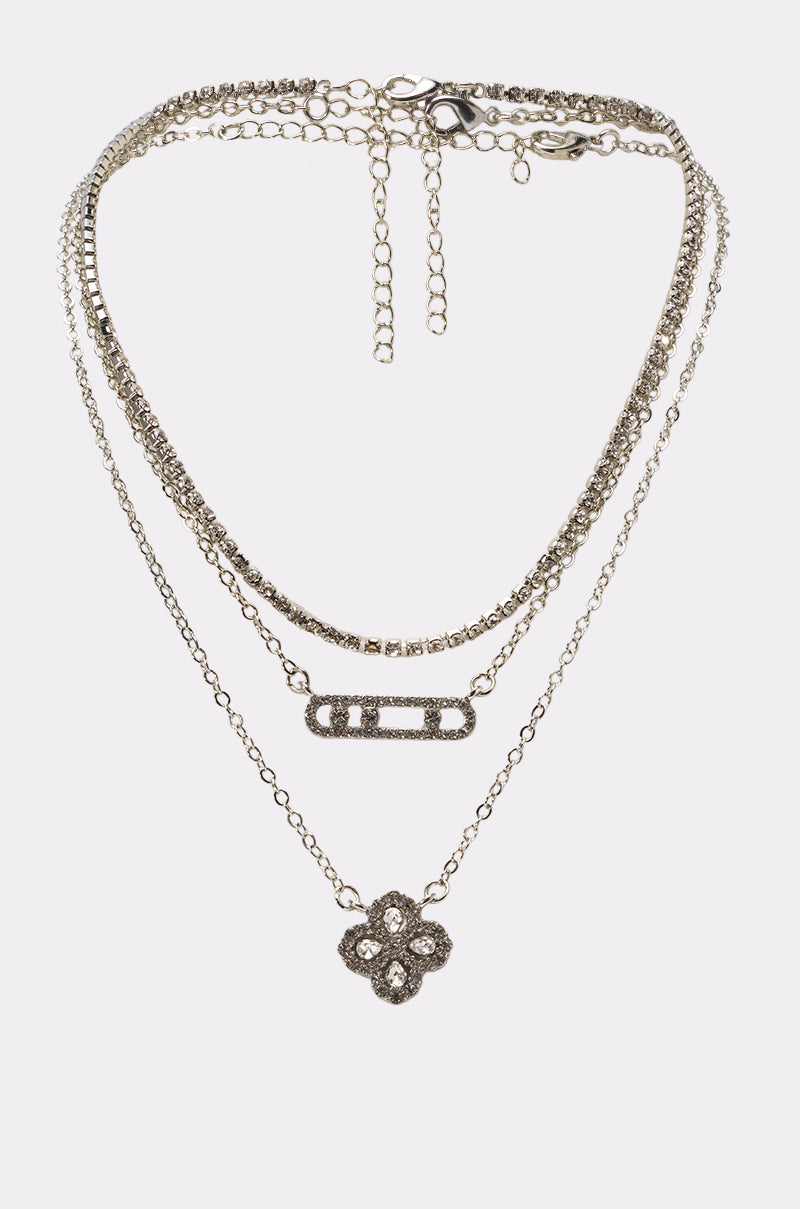 The LUXE LIFE NECKLACE is a layered silver set with four chains: a floral rhinestone pendant, a rectangular rhinestone bar, one simple chain, and one rhinestone chain—all with adjustable clasps.