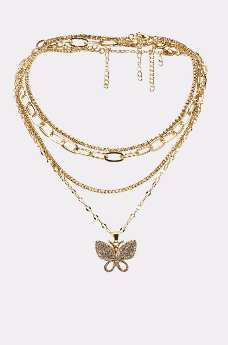 The FLY AWAY NECKLACE showcases layered gold chains and a sparkling butterfly pendant, making it perfect festival jewelry. Displayed on a plain white background.