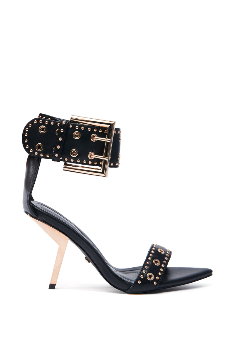 The AZALEA WANG LOBELIA sandal features a sleek black high-heel with a sculpted stiletto, faux leather construction, a large gold buckle, and ornate stud embellishments on the ankle strap for a stylish and edgy look.