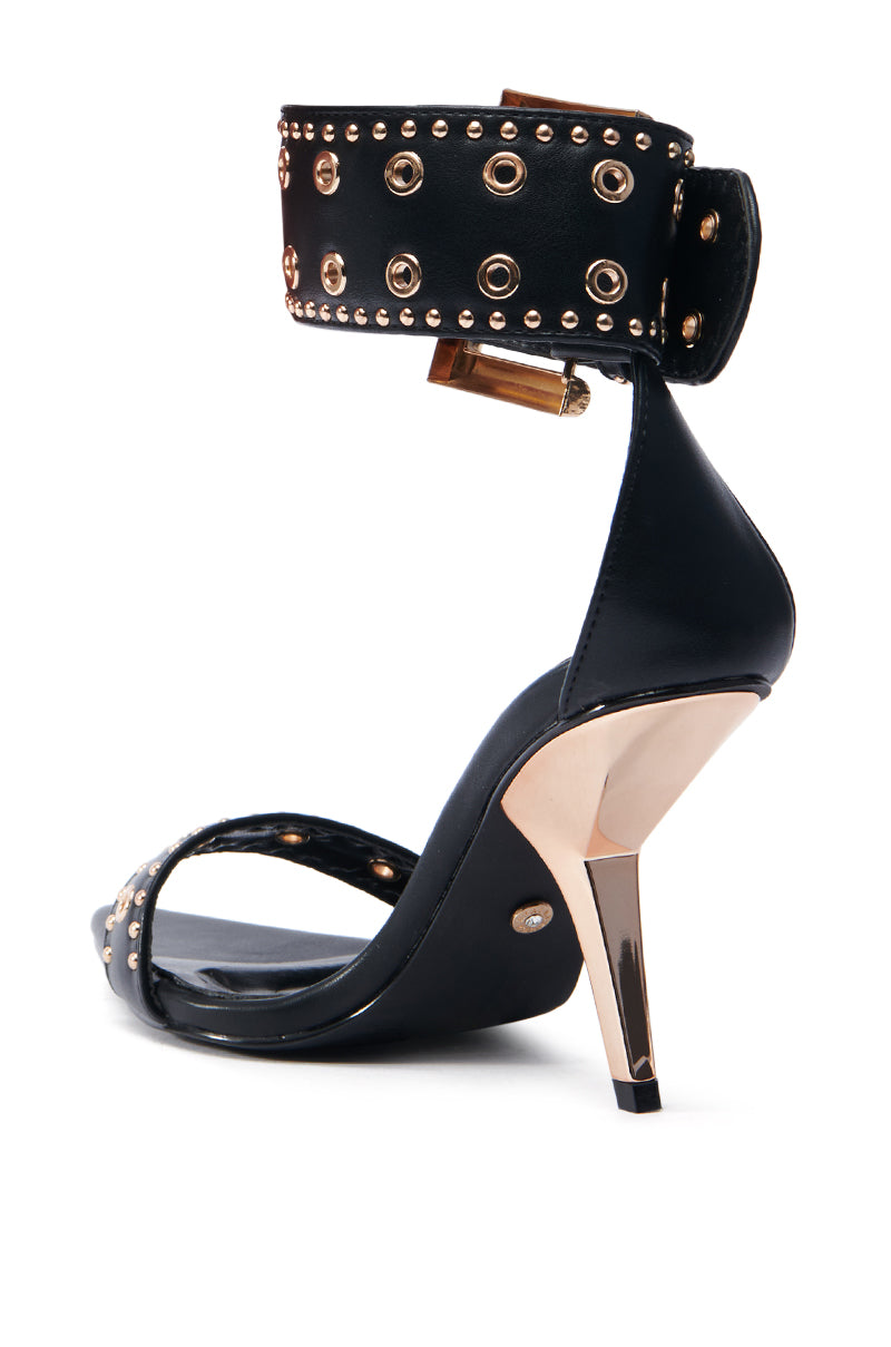 The AZALEA WANG LOBELIA sandal is a stylish faux leather shoe with gold studs, black hardware embellishments, an ankle strap with metallic accents, and a sleek stiletto heel.