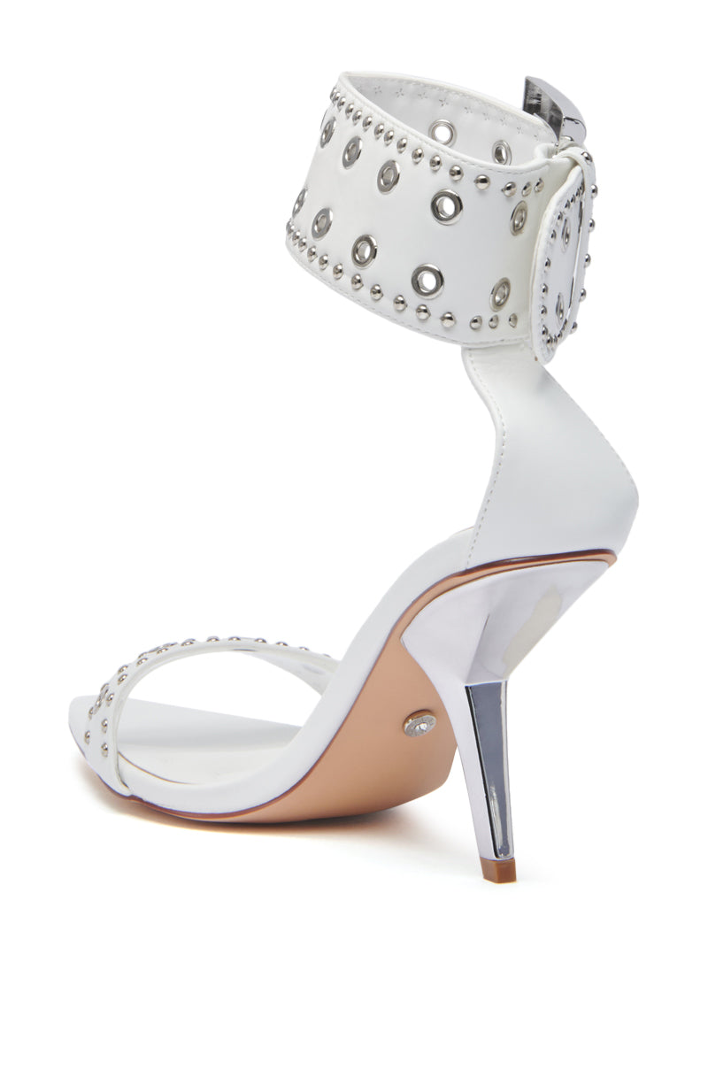 The AZALEA WANG LOBELIA WHITE HARDWARE DETAIL SANDAL features shiny stiletto heels, ankle and toe straps with silver studs and grommets, a tan sole, and is crafted in faux leather for a modern look.