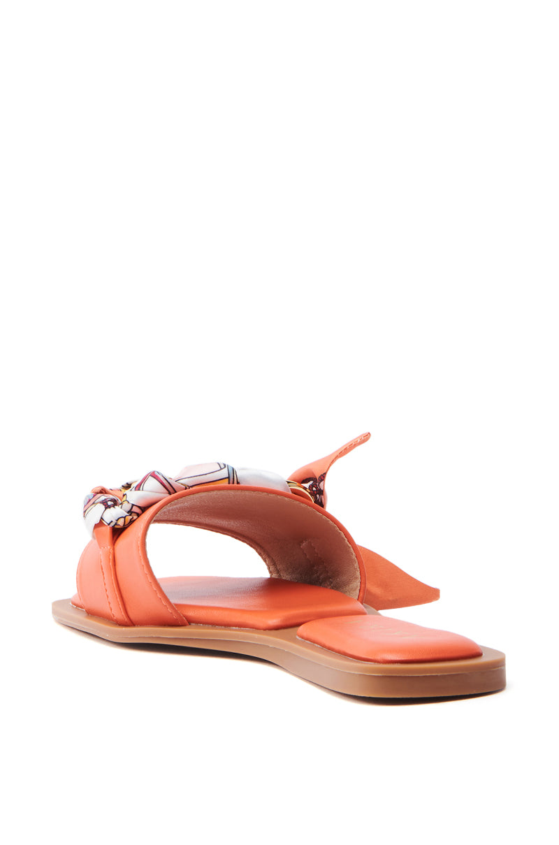 The AKIRA LORCAN ORANGE SANDAL is a vegan leather sandal featuring a flat sole, open square toe, and an ankle strap with a decorative scarf. It displays at a slight angle on a white background.