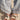 Close-up of a person in light blue ruched wide-leg pants, wearing the AKIRA LORCAN WHITE SANDAL with vegan leather, metallic gold chain, and colorful patterned fabric straps, standing on a light surface.