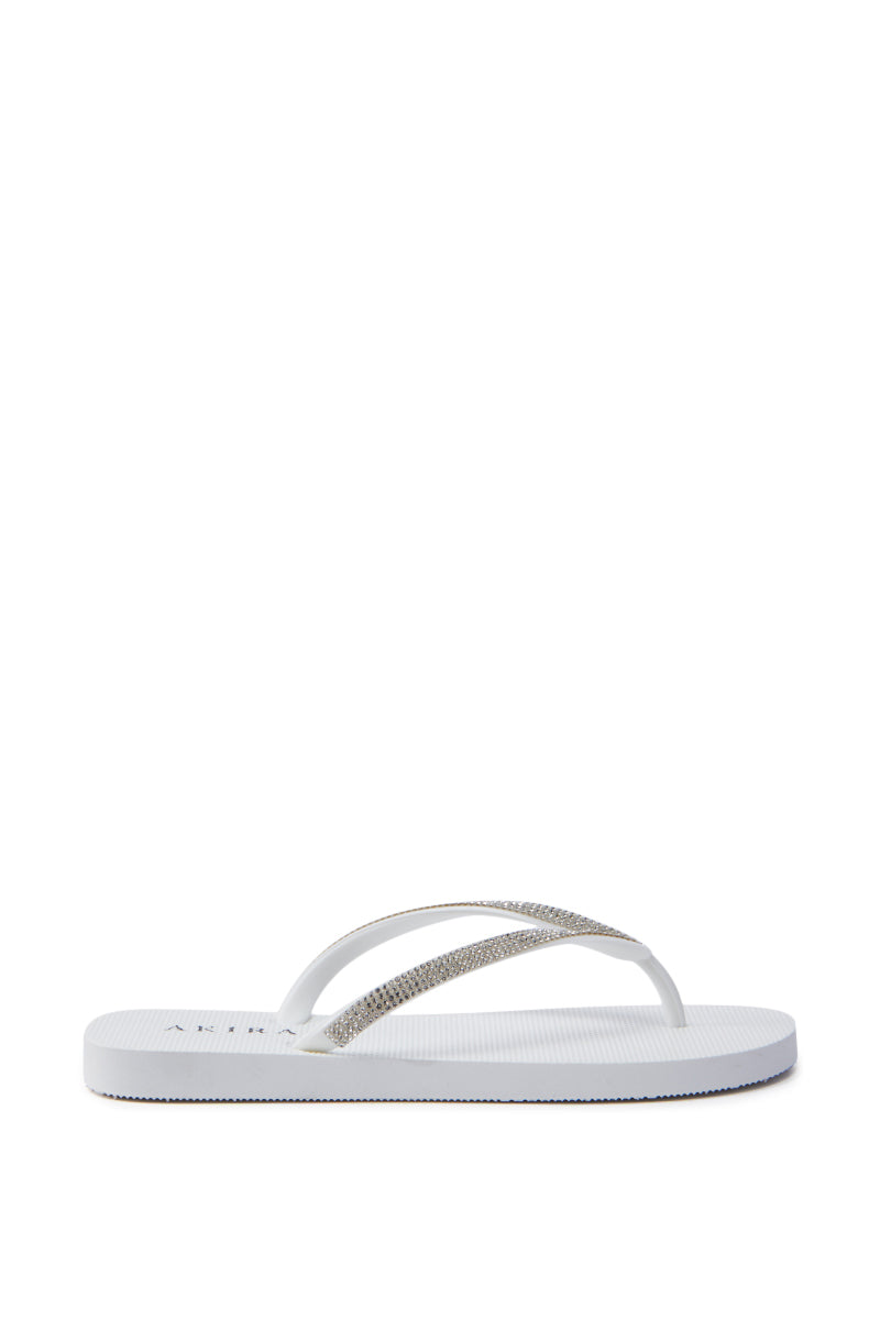 The AKIRA LORETA White Thong Flip Flop features rhinestone-adorned silver straps and a textured PVC sole, presented from the side on a white background.