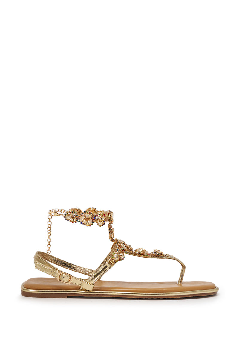 The AZALEA WANG LOSKI Gold Metallic Rhinestone Embellished Flat Strap Sandal features jeweled straps, an ankle chain, side buckle, and a chic square toe, shown against a white background. 2