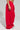 The lower half of a person is visible, showcasing the LOVER OVERSIZED JOGGER in bright red. These loose-fitting pants with a high-rise elastic waistband drape elegantly to the floor, complemented by silver sneakers, all set against a light gray backdrop.