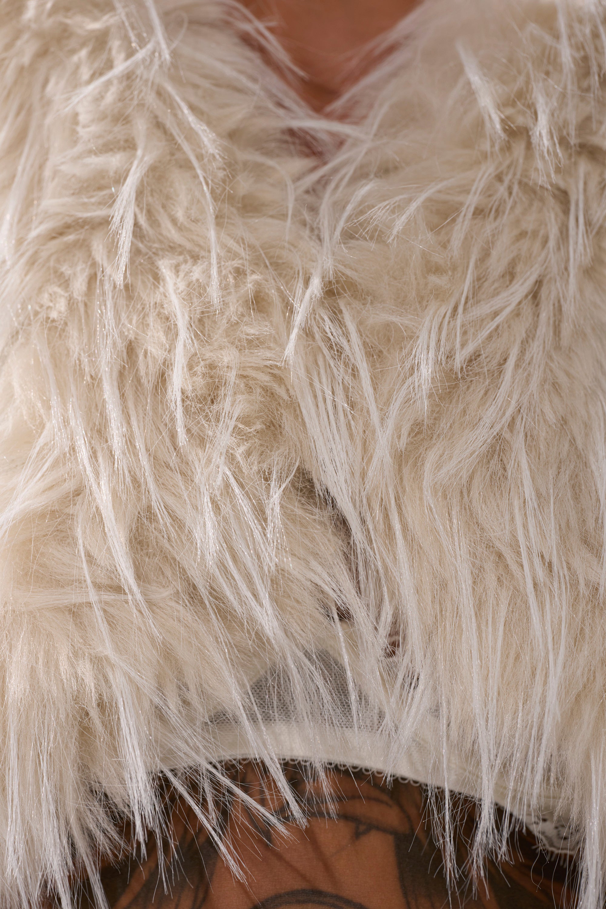Close-up of a person wearing the LOVERGIRL ULTRA CROP FUR TRIM MOTO IN IVORY; fluffy faux fur details, some skin, and a tattoo are partially visible at the bottom of the image.
