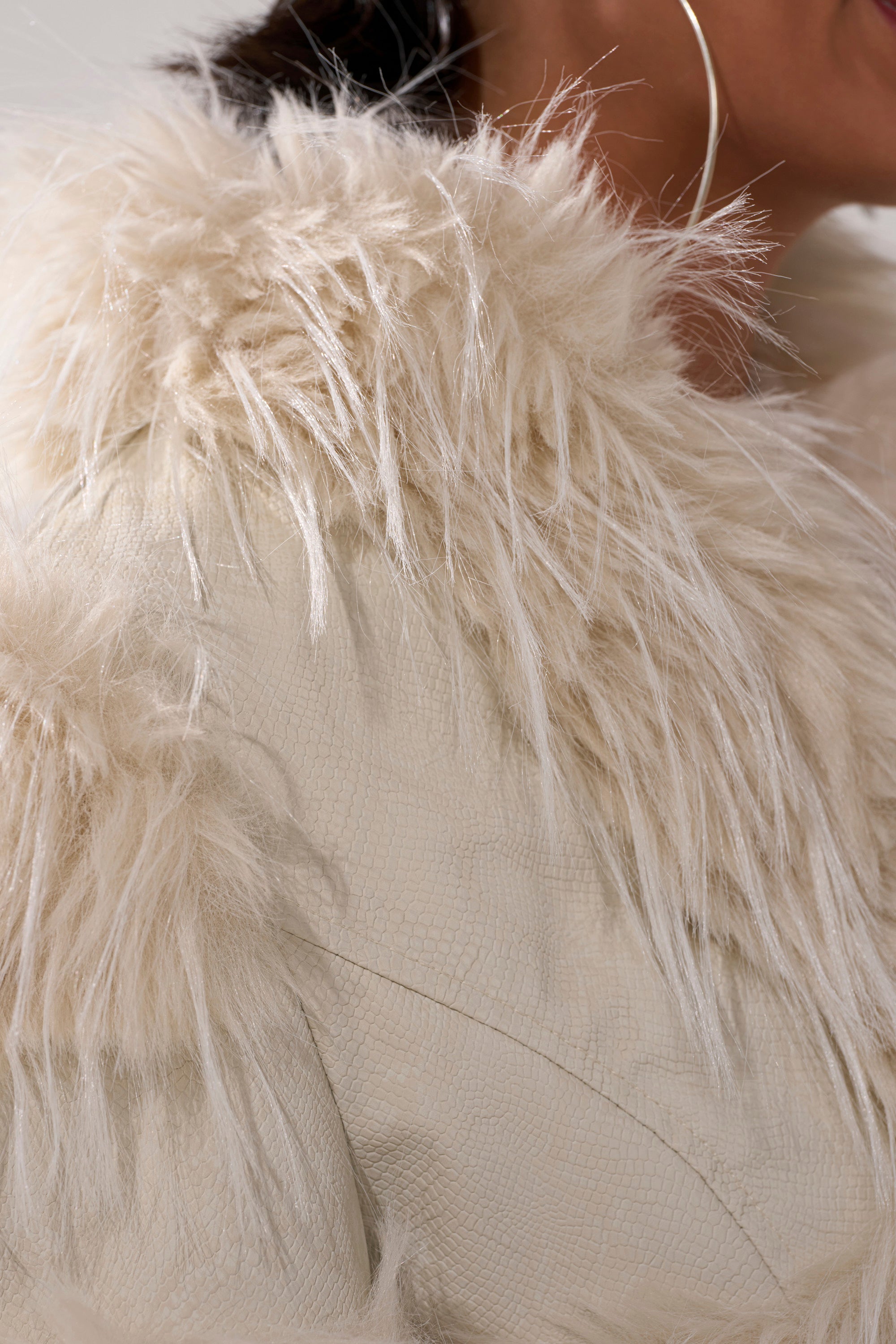 Close-up of a person wearing the LOVERGIRL ULTRA CROP FUR TRIM MOTO IN IVORY, featuring a textured faux fur collar and large hoop earrings that highlight its soft, fluffy details and chic style.