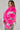 A person with long braided hair poses in the LOVERBOY Faux Fur Moto Jacket in Pink, featuring metallic silver accents, paired with a leopard print skirt. The background is a plain light gray.
