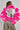 A person with braided hair wears the Loverboy Faux Fur Moto Jacket in Pink, featuring shiny silver fabric with striking pink accents on the shoulders and sleeves. Their stylish ensemble is completed with leopard print pants, set against a plain light gray background.