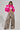 A person wearing the LOVERBOY Faux Fur Moto Jacket in pink, paired with a white crop top and leopard print wide-legged pants, poses confidently against a plain background.