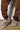 A person wearing brown sweatpants and AZALEA WANG LOVING LEOPARD SANDALS with a cushioned insole stands on a concrete floor.
