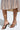 The person is wearing the AKIRA Lowri Brown Snake Spiral Stiletto Sandal, featuring thin, winding straps in a chic snakeskin print. This stylish choice is complemented by a colorful zigzag patterned skirt ending just below the knees, exuding elegance and flair.
