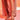 A person stands on a white floor under warm, reddish-orange lighting, wearing a light pink dress and AKIRA LOWRI BROWN SNAKE SPIRAL STILETTO SANDALS. Only their legs and feet are visible.