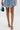 A person in a textured light blue mini dress, holding a small denim handbag, and wearing AZALEA WANG LOWRI DENIM SPARKLE COIL WRAP UP SANDALS stands against a plain white background.