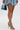 A woman in a textured blue mini dress holds a denim handbag and wears the AZALEA WANG LOWRI DENIM SPARKLE COIL WRAP UP SANDAL, shown from mid-thigh down against a plain white background.