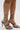 A person wears the AZALEA WANG LOWRI DENIM SPARKLE COIL WRAP UP SANDAL, featuring denim straps with rhinestone embellishments that coil around the ankles and lower legs, and a stiletto heel. The background is plain and light-colored.