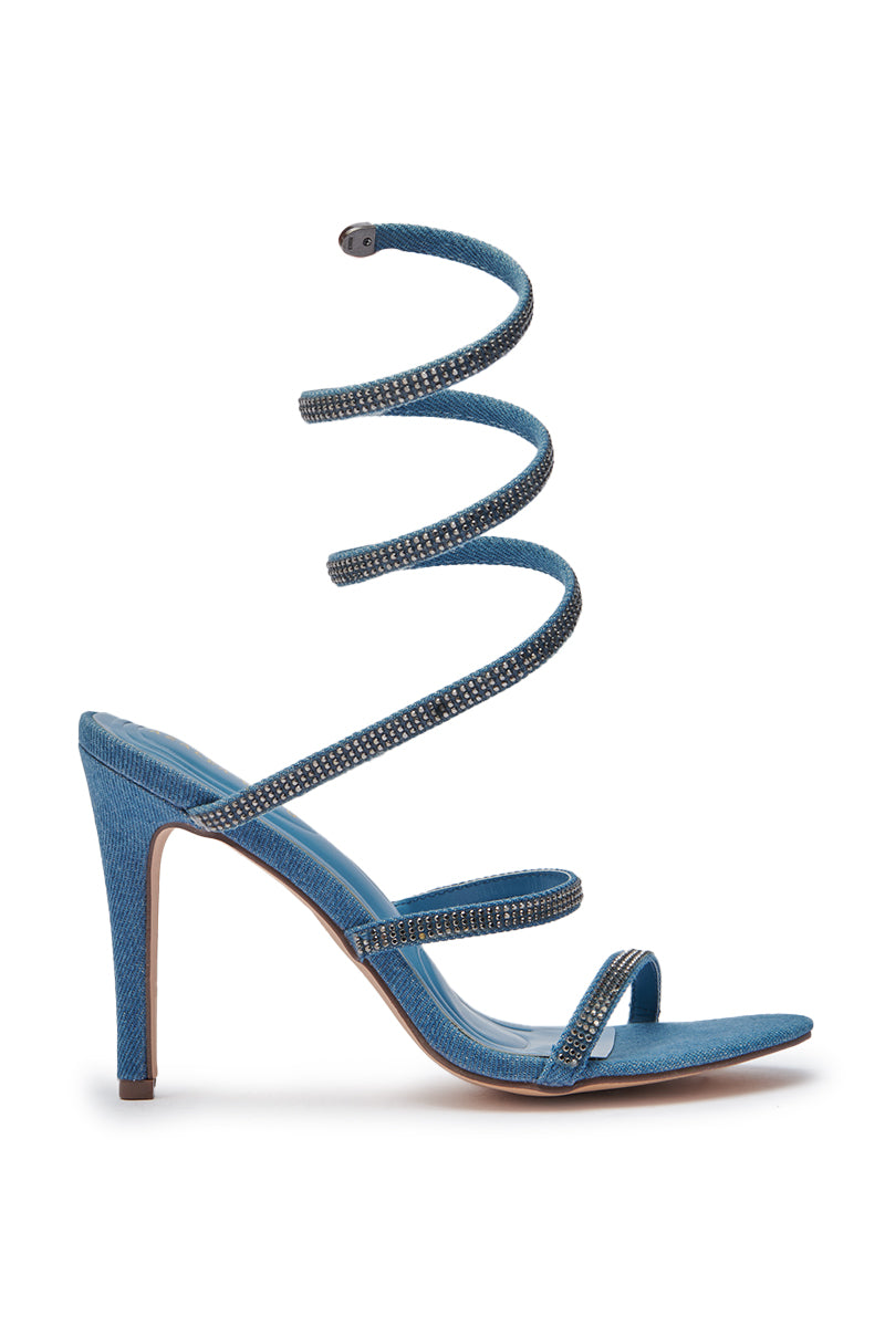 The AZALEA WANG LOWRI DENIM SPARKLE COIL WRAP UP SANDAL features blue denim, two toe straps, a rhinestone-studded spiral ankle strap wrapping up the leg, and a sleek stiletto heel. Shown side view on a white background. 3