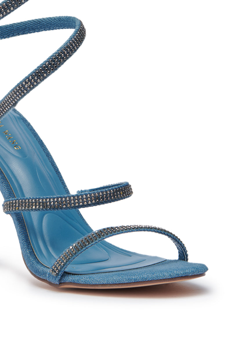 A close-up of the AZALEA WANG LOWRI DENIM SPARKLE COIL WRAP UP SANDAL, a blue denim stiletto with three rhinestone-embellished straps, cushioned insole, open toe, and a striking spiral ankle strap. 6