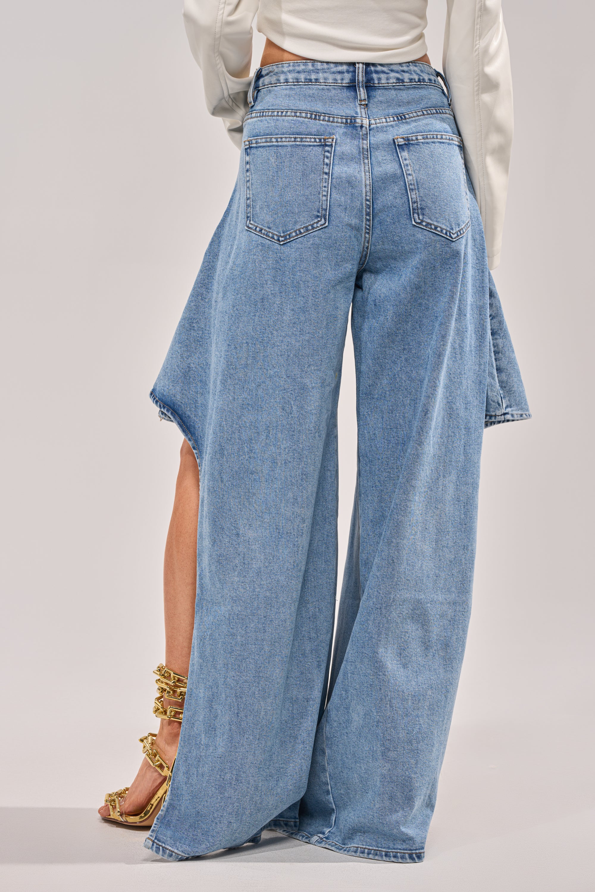 A person is seen from the back wearing CHECK IT OUT RELAXED DENIM—unique medium wash, high-rise flared jeans with side panels and raw hems—paired with gold heels and a white long-sleeve top. 4