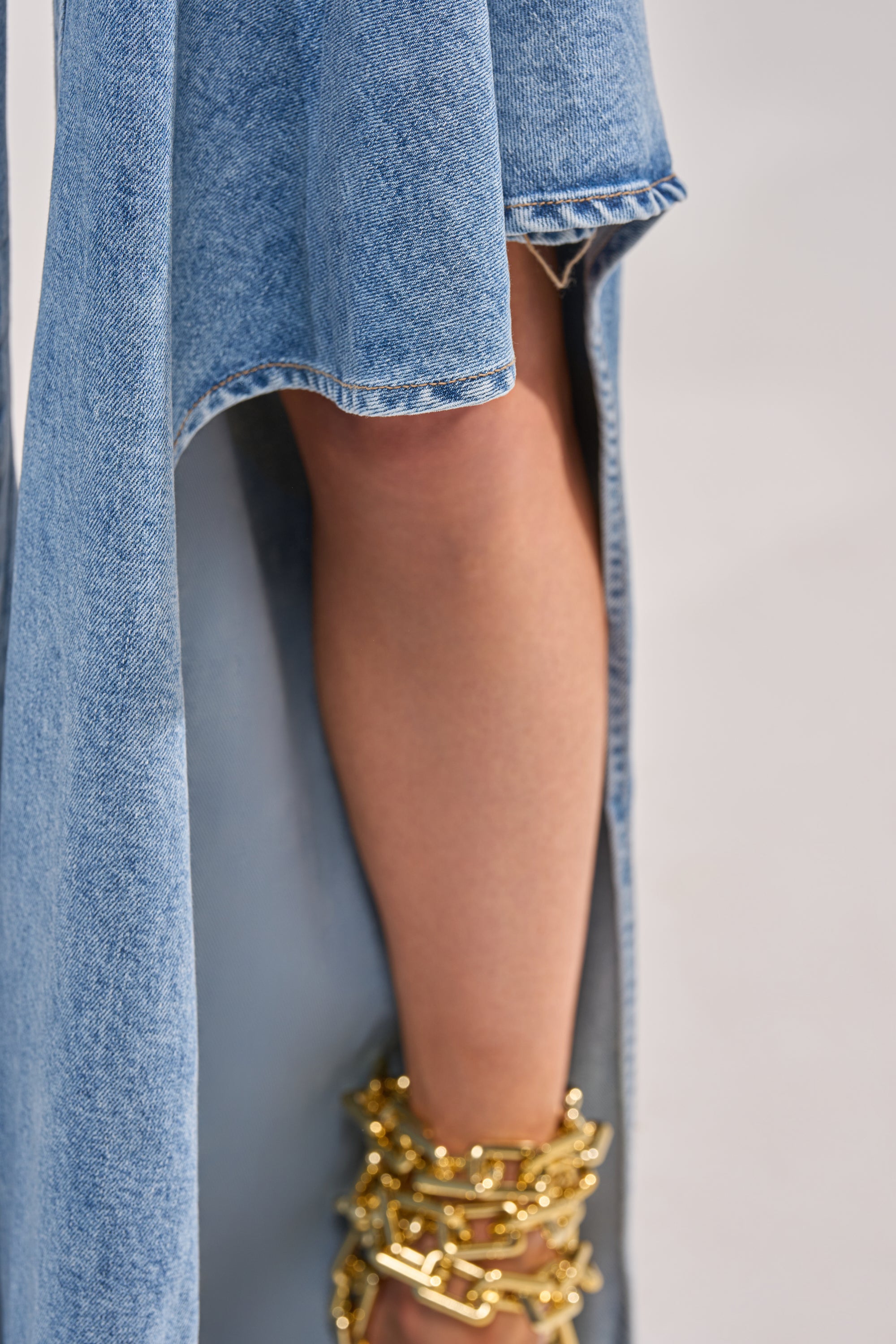 A close-up of a person’s bare leg emerging from the high slit of the CHECK IT OUT RELAXED DENIM skirt, featuring a high-rise waistband and gold chain ankle accessories on their foot. 6