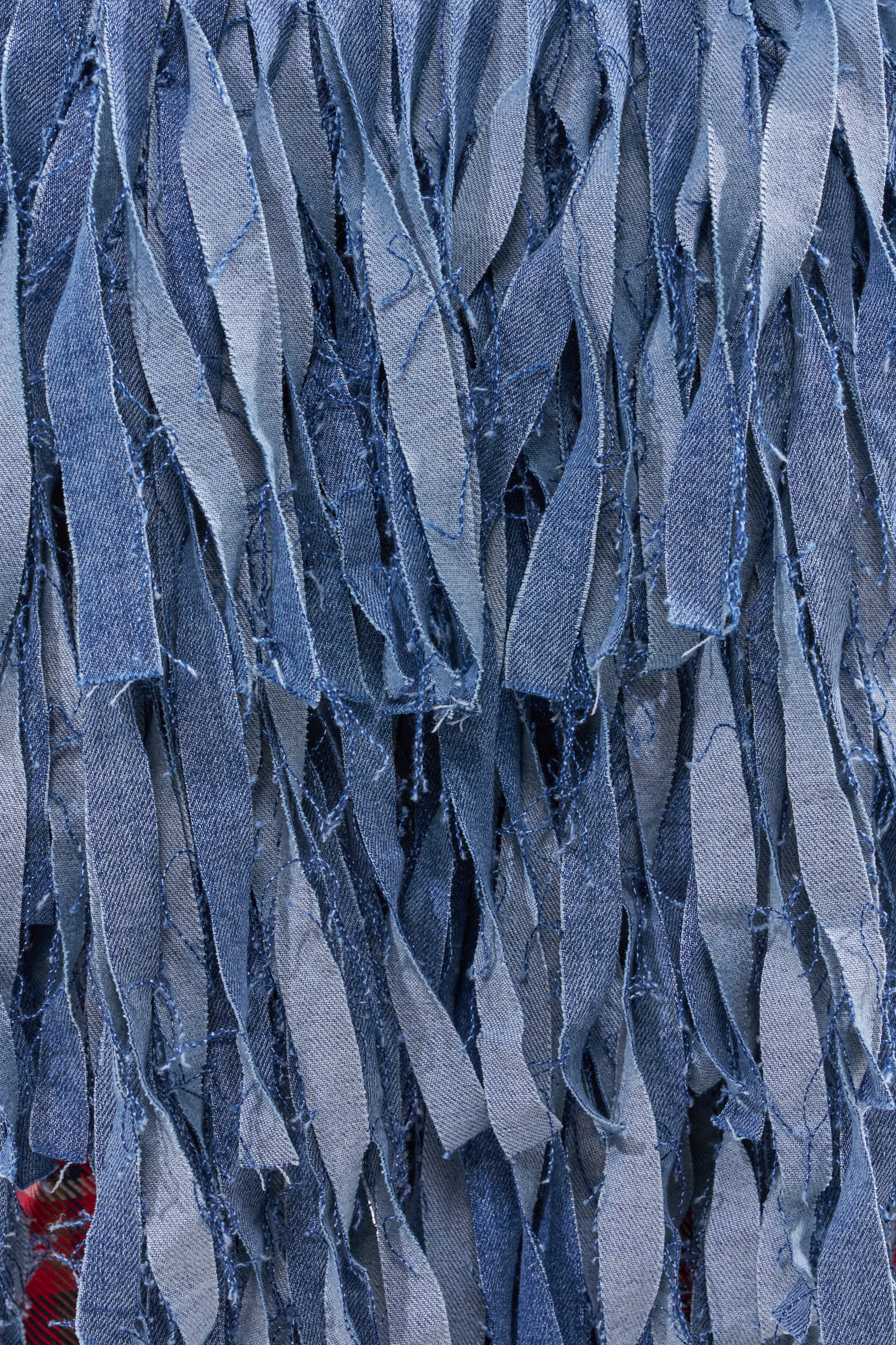 Close-up of many vertical strips of frayed blue denim fabric from the TURN AROUND DISTRESSED DENIM SHORT, showcasing rough edges and varying blue shades for a dynamic, stylishly worn-in look. 7