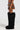 A person wearing the MESS AROUND MINI SKIRT, designed in brown faux leather with striped panel construction, pairs it with large black shaggy boots while standing against a plain background. The image captures this AKIRA Label ensemble from the side view.