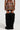 A person wearing a MESS AROUND MINI SKIRT by AKIRA Label, featuring a back zipper, stands with their back turned. They are also wearing tall, black fluffy boots that cover most of their legs. The backdrop is plain and light-colored.