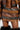 A model wearing the MESS AROUND MINI SKIRT, part of an AKIRA Label patchwork-style ensemble, showcases striped panel construction with brown, tan, and gray sections accented by multiple belt details. The faux leather mini skirt pairs perfectly with the jacket, while black fluffy knee-high boots complete the look.