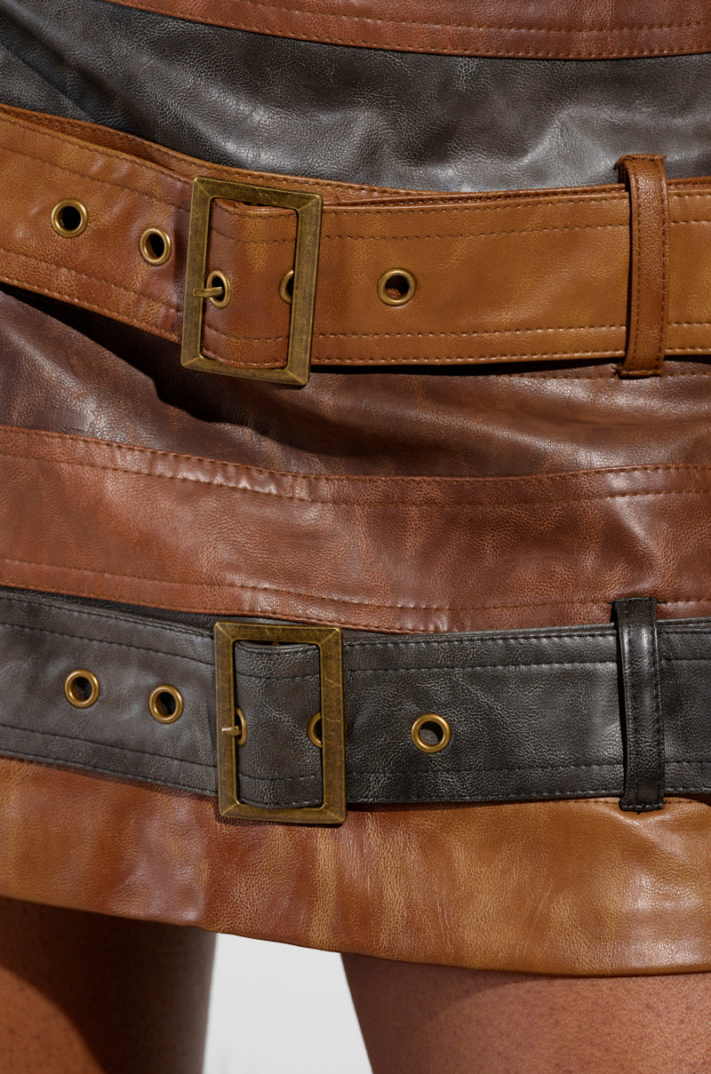 A close-up of the MESS AROUND MINI SKIRT by AKIRA Label features a faux leather mini skirt with striped panel construction in shades of brown and black. The design is highlighted by decorative buckles and eyelets, adding a stylish touch. 4