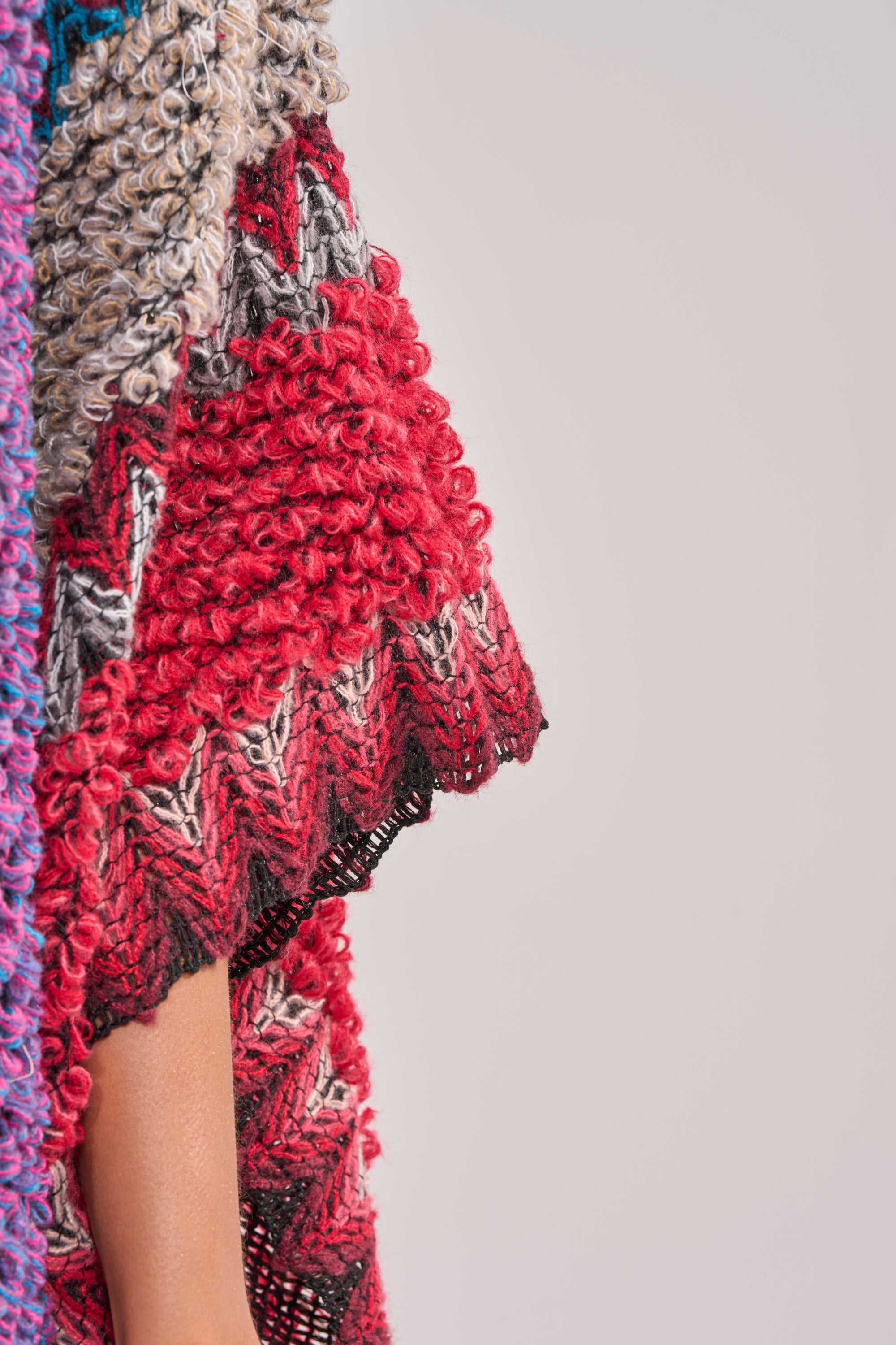 A close-up of the JUST WHAT I AM KIMONO featuring a multi-colored textured knit with red, black, gray, and beige zigzag and curly patterns draped over an arm—ideal for a boho-chic festival look. 3