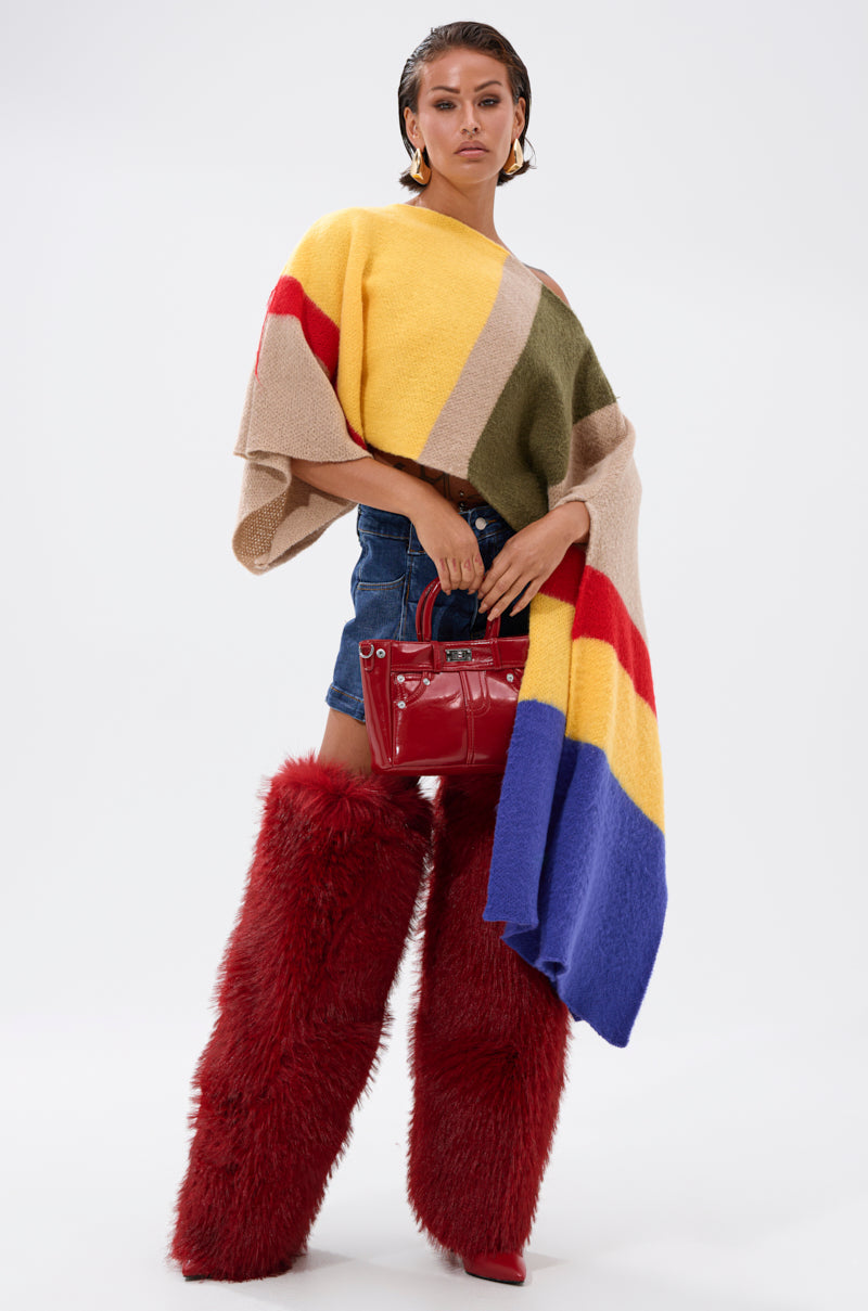 A woman poses in the EASY LOVER CROP ABSTRACT SWEATER featuring bold colorblocking, denim shorts, tall red furry boots, red pointed shoes, and a shiny red handbag.